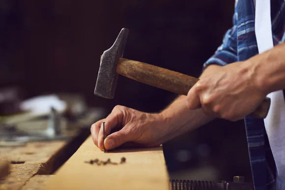 Person schlägt mit einem Hammer ein Nagel in Holz